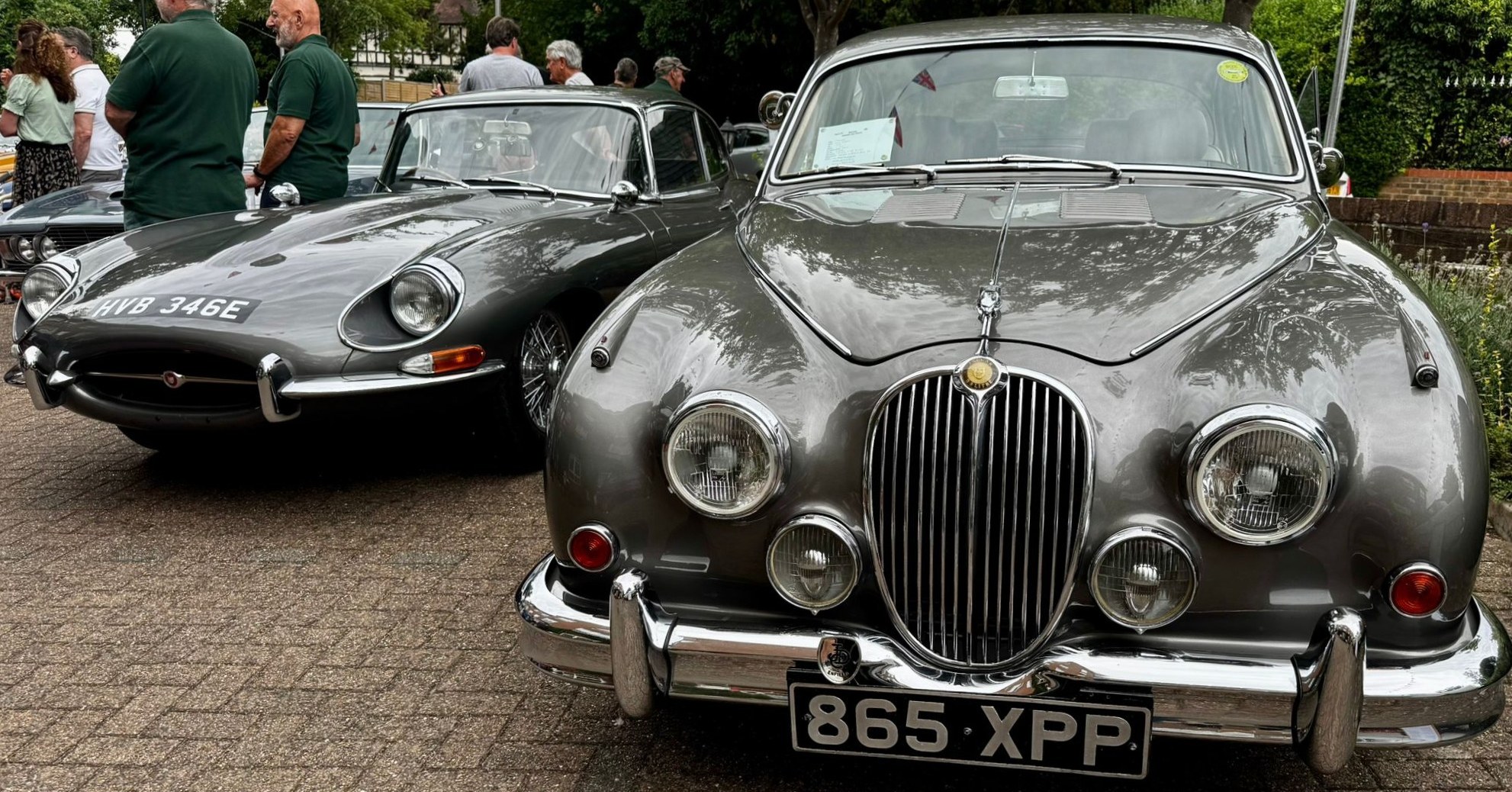Close-up of two grey Jaguar classics at the Springview Care Home Summer Festival in Enfield, admired by residents and visitors.
