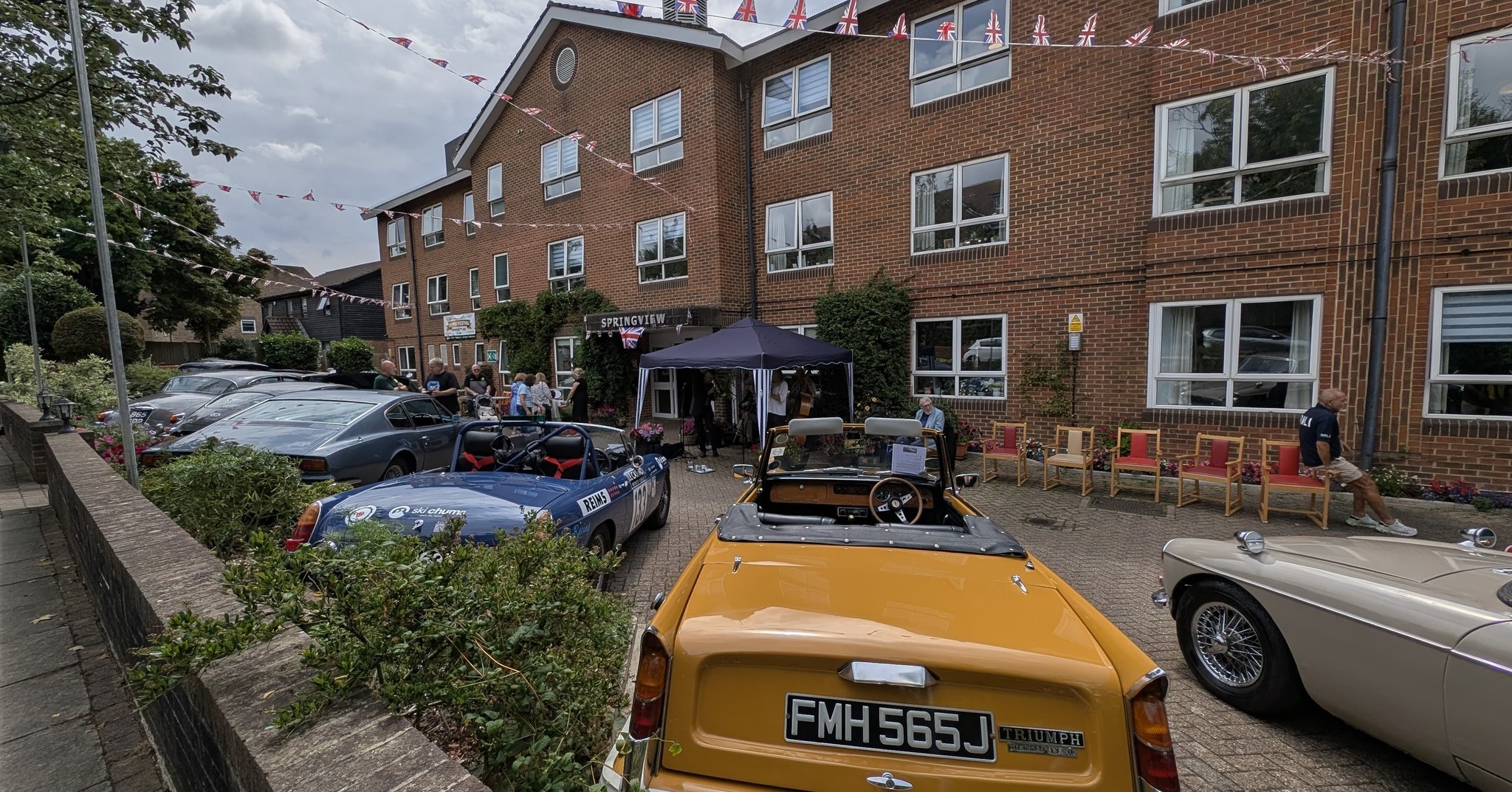Vintage yellow Triumph and other classic cars lined up outside Springview Care Home in Enfield for the Summer Festival.