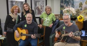 A group of residents and volunteers smiling with two guitarists performing at Spring Grove Care Home for Mitzvah Day.
