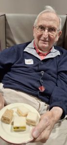 Resident smiling while sampling sandwiches in Spring Lane Care Home lounge.