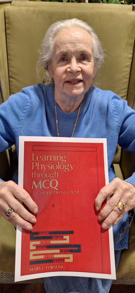 Resident holding a book on physiology during Women in Science Day activity at Spring Lane Care Home in North London