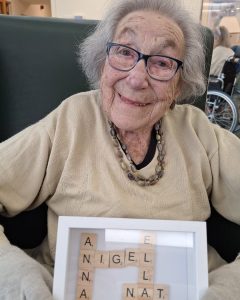 Resident holding a Scrabble tile display featuring a meaningful word at Spring Grove Care Home.