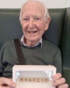 Resident smiling while displaying creative Scrabble artwork at Spring Grove in Hampstead.