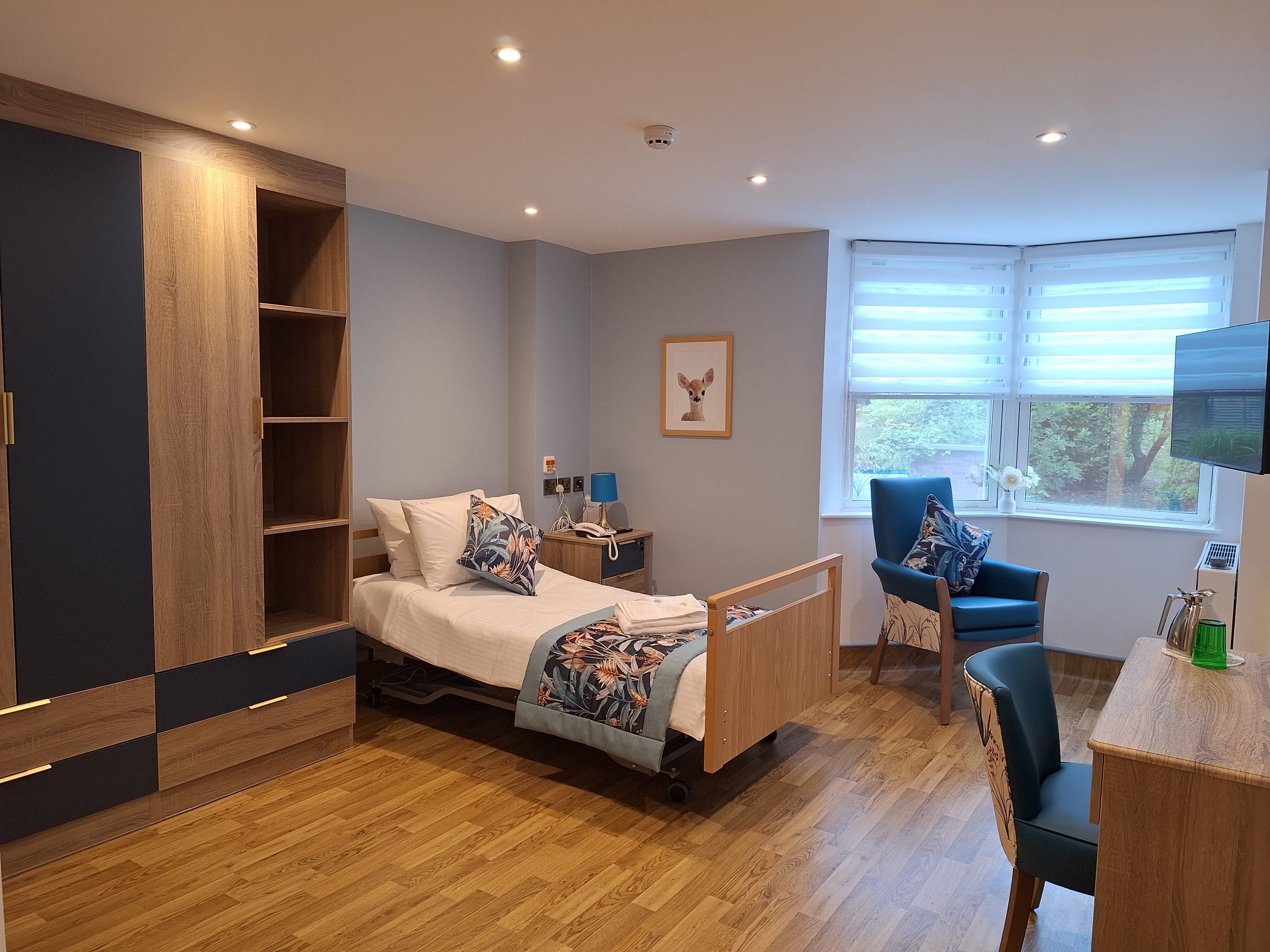 Bright and comfortable en-suite bedroom at Spring Grove Care Home with fitted furniture and seating area.